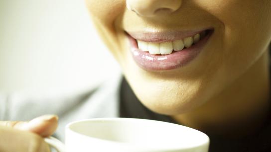 A woman smiles while holding a coffee cup