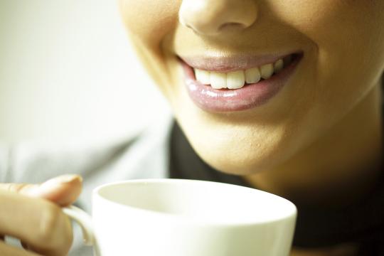 A woman smiles while holding a coffee cup